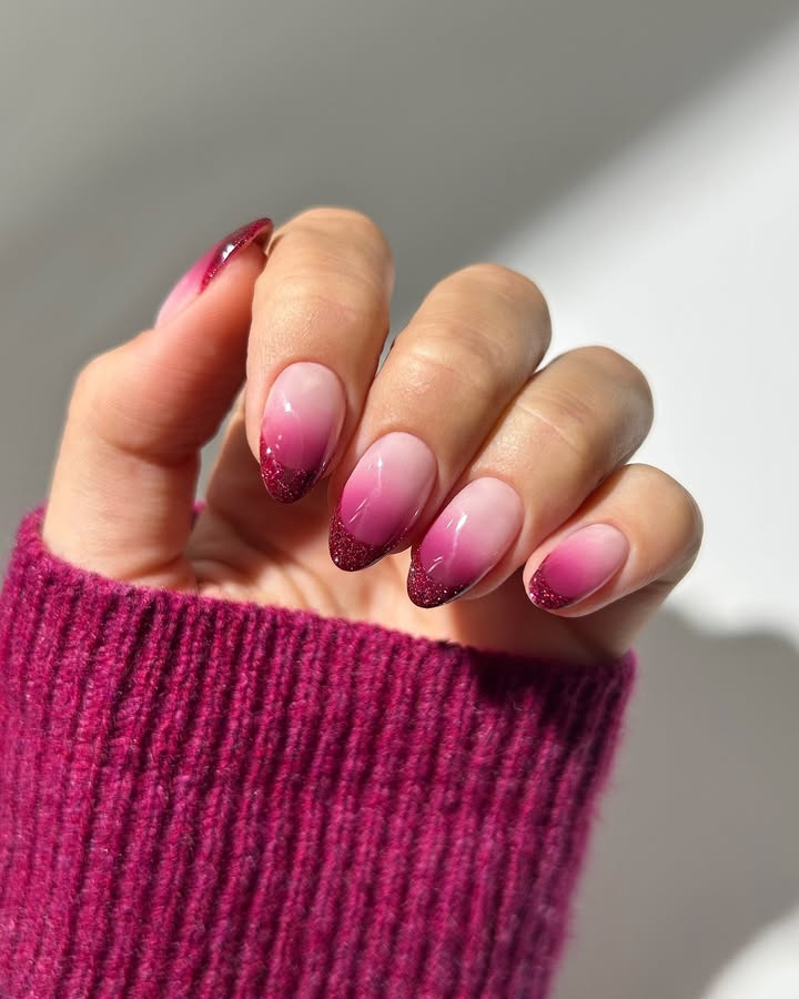 Close-up-of-a-hand-with-elegant-ombre-nails-featuring-a-gradient-from-soft-pink-to-deep-burgundy-with-a-glittery-tip-paired-with-a-matching-burgundy-sweater.jpg