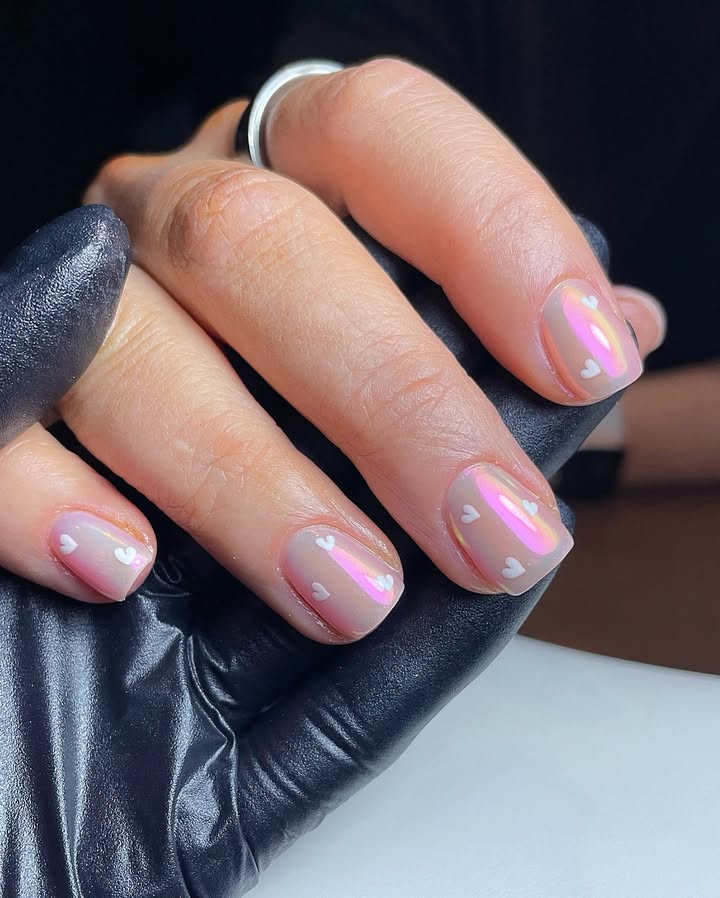 Close-up of hand with blush chrome nails featuring baby heart designs.jpg