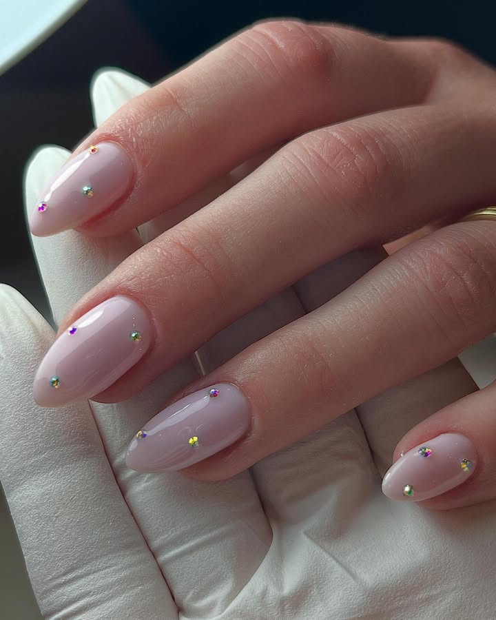 Close-up-of-hand-with-creamy-pink-nails-adorned-with-tiny-holographic-crystals-and-a-glossy-finish.jpg