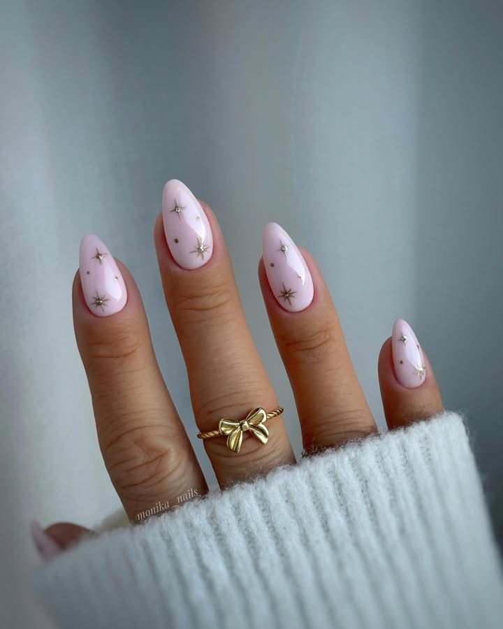 Close-up-of-hand-with-milky-pink-almond-nails-featuring-golden-dust-and-tiny-stars-paired-with-rings-and-a-white-outfit.jpg