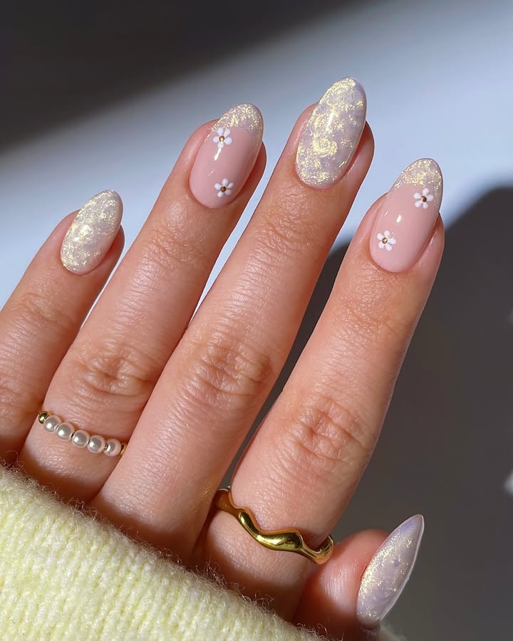 Close-up-of-hand-with-nude-base-nails-featuring-golden-sparkles-and-petite-daisies-paired-with-rings-and-a-yellow-outfit.jpg