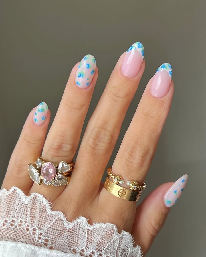 Close-up-of-hand-with-pink-base-spring-nails-featuring-blue-and-green-artistic-splashes-paired-with-rings-and-a-white-outfit.jpg