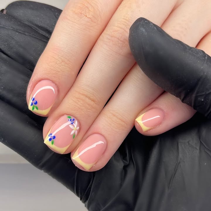 Close-up-of-hand-with-yellow-French-tips-and-hand-painted-blue-and-white-floral-accents-with-green-leaves.jpg