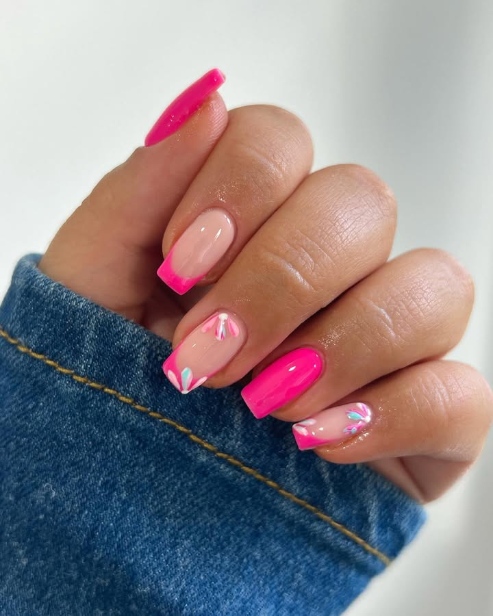Hands-with-neon-pink-French-tip-nails-adorned-with-delicate-white-and-pastel-floral-accents-paired-with-a-blue-shirt.jpg