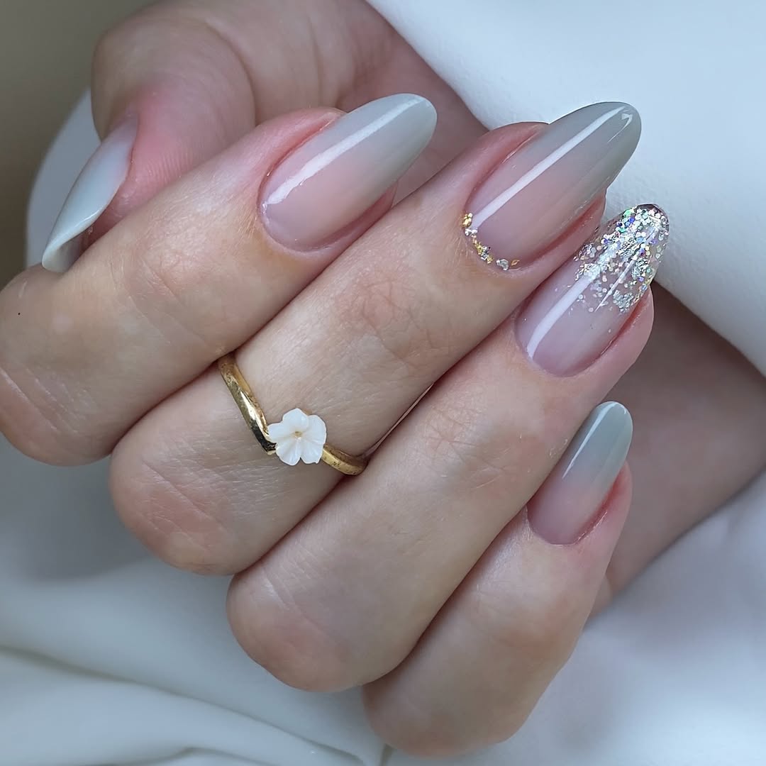 Stiletto-almond-nails-with-a-nude-pink-to-gray-gradient-paired-with-a-ring-and-soft-golden-light.jpg