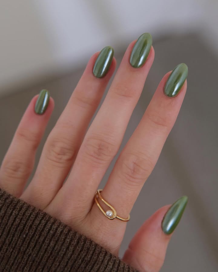 Close-up-of-long-almond-shaped-nails-with-olive-chrome-polish-and-a-subtle-cat-eye-shimmer-paired-with-ring-and-black-outfit.jpg